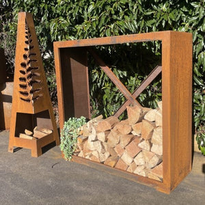 Rust-colored metal firewood holder with stacked firewood against a green bush background